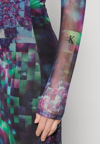 Robe colorée et moulante avec un motif numérique en pixels dans des teintes de violet, vert et bleu. Comprend un matériau transparent et un détail de logo sur la manche.