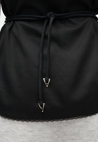 Μαύρο ύφασμα δεμένο στη μέση με λεπτό κορδόνι που έχει ασημί τρίγωνα μεταλλικά άκρα, πάνω από ένα γκρι πλεκτό ένδυμα με υφή και δαντελένιο τελείωμα.