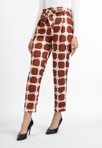 Bruin en ivoorkleurige geblokte broek met een ceintuur in de taille, gemaakt van een glanzende stof, met een taps toelopende pijp en gezoomde manchetten. Een paar zwarte hoge hakken.
