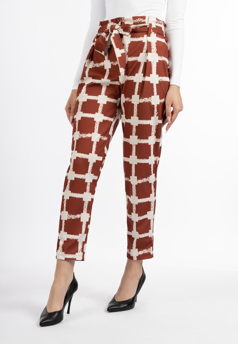 Bruin en ivoorkleurige geblokte broek met een ceintuur in de taille, gemaakt van een glanzende stof, met een taps toelopende pijp en gezoomde manchetten. Een paar zwarte hoge hakken.