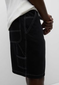 Short en denim noir avec surpiqûres blanches contrastées, poches latérales et coupe droite. Le tissu présente une texture lisse.