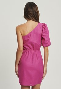 Robe asymétrique en tissu rose vif, avec une taille cintrée et un détail de manche bouffante, mettant en avant une texture lisse et un design simple.