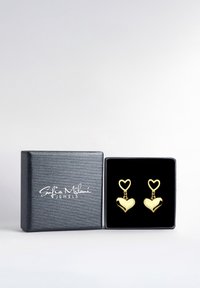 Goldfarbene, herzförmige Ohrringe hängen an herzförmigen Haken und sind in einer mit schwarzem Samt ausgekleideten Schmuckschatulle mit strukturiertem silbernem Äußeren präsentiert.