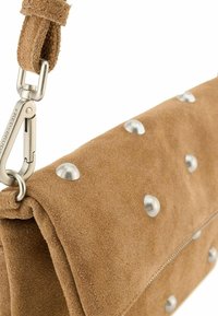 Pochette in suede marrone con borchie metalliche argentate. Il design con patta presenta una cerniera visibile e una strap a clip per il fissaggio.