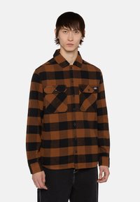 Brun og sortternet skjorte med lange ærmer, knaplukning foran og to brystlommer. Fremstillet af stof med flanneltekstur.
