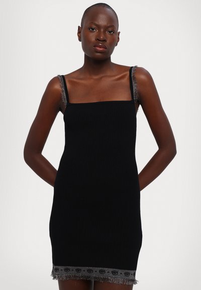Robe noire côtelée avec bretelles ajustables, dotée d'un ourlet à franges grises et d'un motif décoratif le long du bord. Design ajusté.