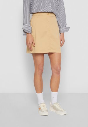 Jupe kaki à coupe droite, fabriquée en coton. Caractéristiques : fermeture à bouton et détail de poches, accompagnée de chaussettes blanches et de baskets beiges.