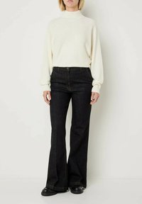 Maglione color crema con collo alto e dettagli a coste, abbinato a jeans a vita alta in denim scuro a campana. Scarpe chunky nere completano il look.
