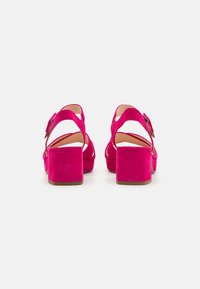 Roze suede hakken sandalen met een chunky blockhak, open achterkant en banddetails. Soepele textuur met een effen kleur en minimale accenten.