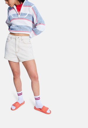 Farebný krátky sveter s modrými, bielymi a ružovými pruhmi, kombinovaný s vysokými béžovými šortkami. Nosené s bielymi ponožkami a oranžovými šľapkami.