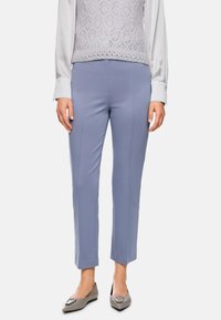 Hellblaue, maßgeschneiderte Hose mit glatter Textur, Seitennähten und slim-fit Design, kombiniert mit grauen Ballerinas und einem strukturierten, hellen Oberteil.