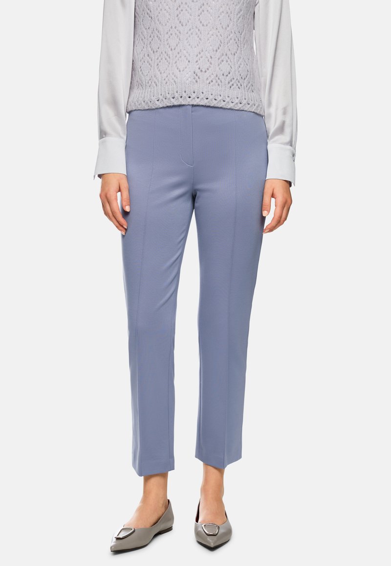 Hellblaue, maßgeschneiderte Hose mit glatter Textur, Seitennähten und slim-fit Design, kombiniert mit grauen Ballerinas und einem strukturierten, hellen Oberteil.