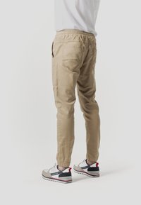 Pantalones jogger khaki con cinturilla elástica, dos bolsillos traseros y piernas ajustadas. Combinados con zapatillas deportivas multicolor.