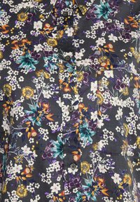 Blommig skjorta med knappar och mörk bakgrund, dekorerad med vita, lila och orange blommor. Inkluderar en ficka och texturerad tyg.