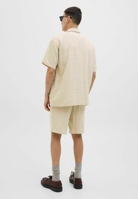 Conjunto de camisa de manga corta y pantalones cortos en tejido texturizado de color beige claro. Combinado con calcetines grises y zapatos de cordones marrones. Corte simple y relajado.