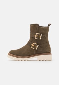Bottines en daim vert avec deux boucles en or, semelle épaisse beige et coutures le long des bords.