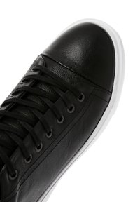 Sneaker in pelle nera con punta arrotondata, suola in gomma bianca e lacci neri. Presenta una parte superiore con texture e occhielli metallici per i lacci.