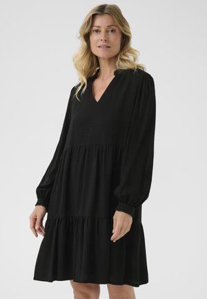 Robe noire à volants avec de longues manches bouffantes, décolleté en V, texture côtelée et poignets volants. Design fluide avec une coupe décontractée.