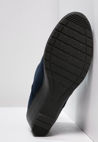 Chaussure en suède marine avec une semelle épaisse en caoutchouc noir dotée d'une semelle crantée texturée pour une meilleure adhérence. Conçue avec un bout arrondi et un style sans lacets.