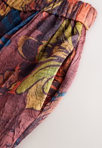 Pantalon léger en tissu multicolore avec taille élastique et texture froissée, arborant des motifs abstraits audacieux en rouge, vert et bleu.