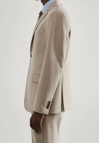 Beige pak met een getailleerd ontwerp, enkele knoopsluiting, notch revers en een linkse borstzak. Rechte broek met platte voorkant maakt de look compleet.