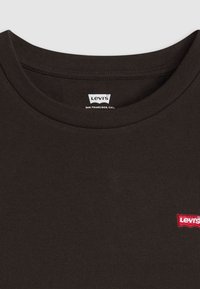 Camiseta preta de algodão com gola redonda. Apresenta um patch vermelho com o logótipo da Levi's cosido no peito esquerdo. Textura suave, vista de perto.