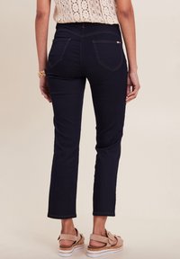 Navyblauwe denim jeans met een slim fit, een gemiddelde taillehoogte en subtiele stikdetails op de achterzakken, gecombineerd met lichtgekleurde sandalen.