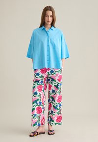 Camisa azul claro de gran tamaño con mangas cortas y un bolsillo en el pecho, combinada con pantalones de pierna ancha con un patrón floral en rosa, verde y azul.