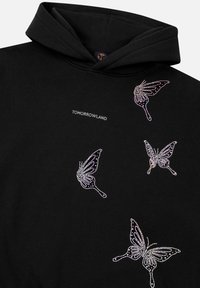 Zwarte hoodie met kristalversieringen in de vorm van vlinders in zilver en roze, met de tekst "TOMORROWLAND" boven de afbeeldingen.