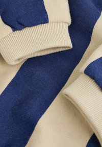 Close-up of blue and beige striped fabric with ribbed knit cuffs, showing soft texture and folded garment details.
