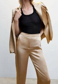 Pantalones de satén beige con una textura suave, combinados con una camiseta de tirantes ajustada negra. El blazer beige está colgado sobre un hombro.