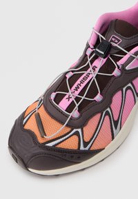 Sapatilha de corrida com um cabedal em malha castanha, detalhes em rosa e laranja, pormenores refletivos, atacadores elásticos e uma sola almofadada.