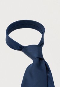 Granatowy jedwabny krawat o gładkiej fakturze z subtelnym wzorem w okolicy kołnierzyka, starannie zawiązany na środku.