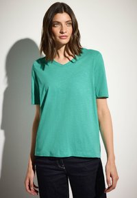 Turkos t-shirt med v-ringning och korta ärmar, med en mjuk textur och avslappnad passform, kombinerad med mörka jeans.