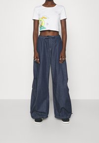 Vit, kort t-shirt med färggrafisk design, kombinerad med lösa, mörka denimbyxor med elastisk mudd och dragsko i midjan.