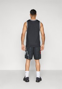 Čierny bezrukávový športový top s bielym lemovaním, v kombinácii s čiernymi šortkami so červeným akcentom a vzorom blesku, bielymi ponožkami a čiernymi topánkami.