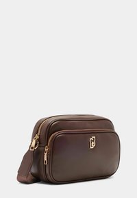 Hnědá kožená crossbody taška se zlatými kovovými prvky, která má dvě zipové přihrádky a strukturovaný popruh. Logo detail na přední straně.