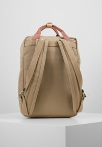 Brązowy plecak z wyściełanymi paskami i uchwytem u góry. Posiada gładką fakturę i wyeksponowane przeszycia. Minimalistyczny design, bez widocznych logo.