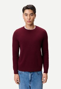 Vinröd stickad tröja med ribbad struktur, rund halsringning och långa ärmar, kombinerad med ljusblå denimjeans.