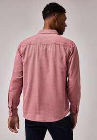 Camicia rossa con bottone, in tessuto dalla trama testurizzata, maniche lunghe e polsini con bottone, con orlo curvo e dettagli del giogo posteriore.