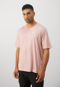 T-shirt rosa chiaro a maniche corte con un discreto logo bianco sul petto. Realizzato in tessuto morbido e traspirante con una vestibilità rilassata.
