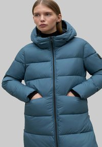 Abrigo acolchado con capucha en color azul verdoso con un diseño acolchado, que cuenta con una cremallera delantera y bolsillos laterales. Textura suave y ajuste casual.