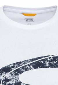 Hvid bomulds T-shirt med rund hals, der har et stort mørkeblå grafisk design med en tekstureret overflade og en lille gul akcent ved kraven.