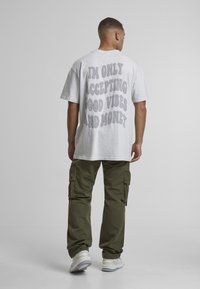 Gray cotton t-shirt with oversized design featuring white text on the back, paired with green cargo pants and white sneakers.