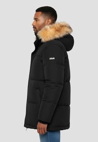 Sort pufferjakke med en hætte med pelskant, udstyret med lynlåslukning og sidelommer, lavet af tekstureret, isolerende materiale.