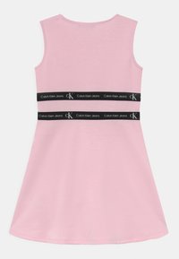 Jasnoróżowa sukienka bez rękawów o rozszerzanym kształcie, z czarnym pasem z logo "Calvin Klein Jeans" wokół talii. Miękka tekstura materiału.