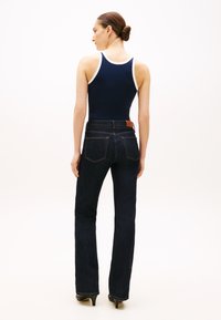 Ναυτικό μπλουζάκι χωρίς μανίκια με λευκή επένδυση, συνδυασμένο με σκούρο τζιν παντελόνι με φαρδιά μπατζάκια. Σημαντικές λεπτομέρειες είναι οι ραμμένες τσέπες και το καφέ δερμάτινο ταμπελάκι στη ζώνη μέσης.