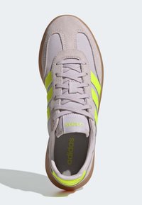 Light gray suede athletic shoe with neon green stripes, round toe, and textured mesh lining. Features flat laces and a brown rubber sole.