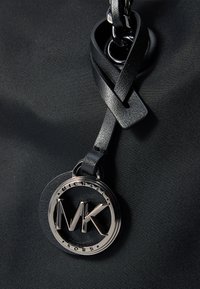 Borsa in tessuto nera con un charm logo MK in tonalità argento, dettagli in pelle intrecciata e design circolare. Texture liscia e finitura elegante.
