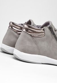 Chaussures en simili cuir gris avec des accents métalliques, une finition texturée, une fermeture éclair sur le côté et une semelle en caoutchouc blanche, présentant une forme arrondie.